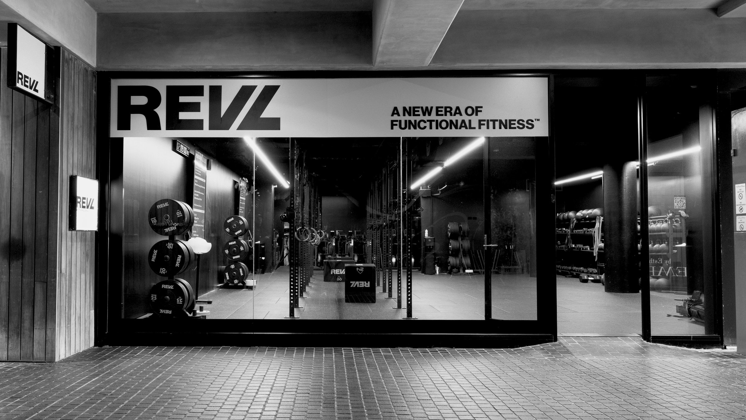 A REVL studio shopfront at night, the lit fascia above full-height glass with the training floor inside